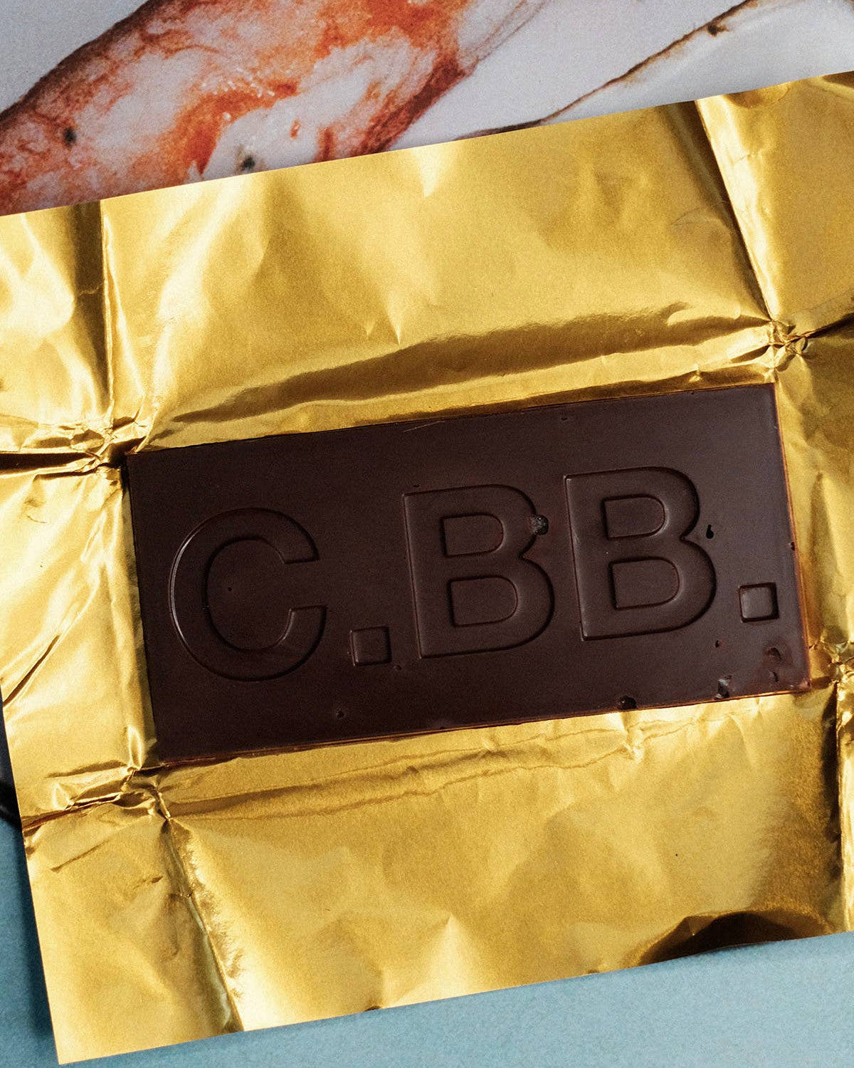 Chocolate bar with gold wrapper labeled 'C.B.B.' on a white plate with fish.
