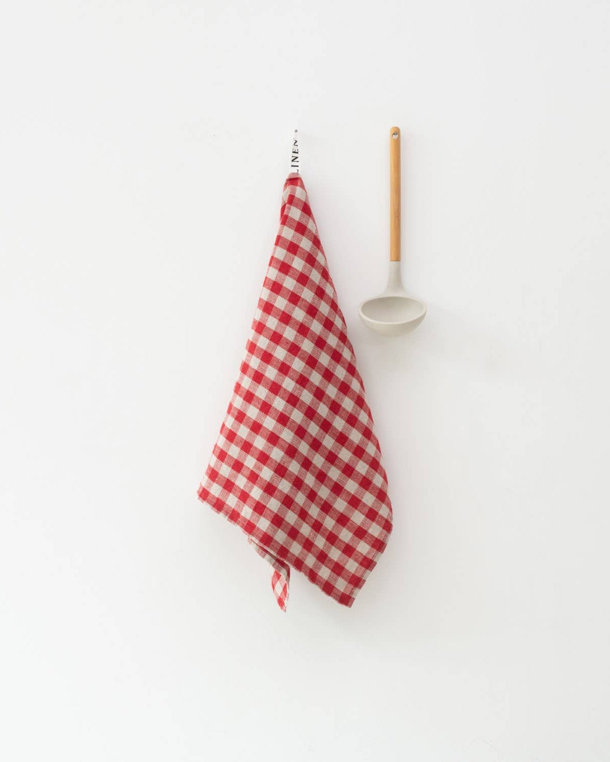 Red and white checkered towel hanging on a hook with a white wall background