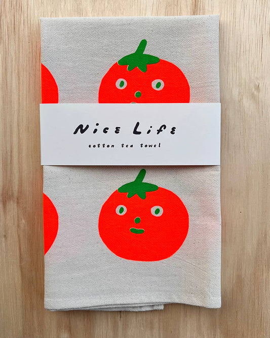 Folded tea towel with tomato design and 'Nice Life' label on a wooden surface