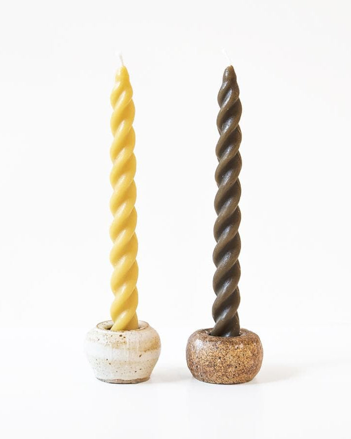 Two twisted candles in ceramic holders on a white background