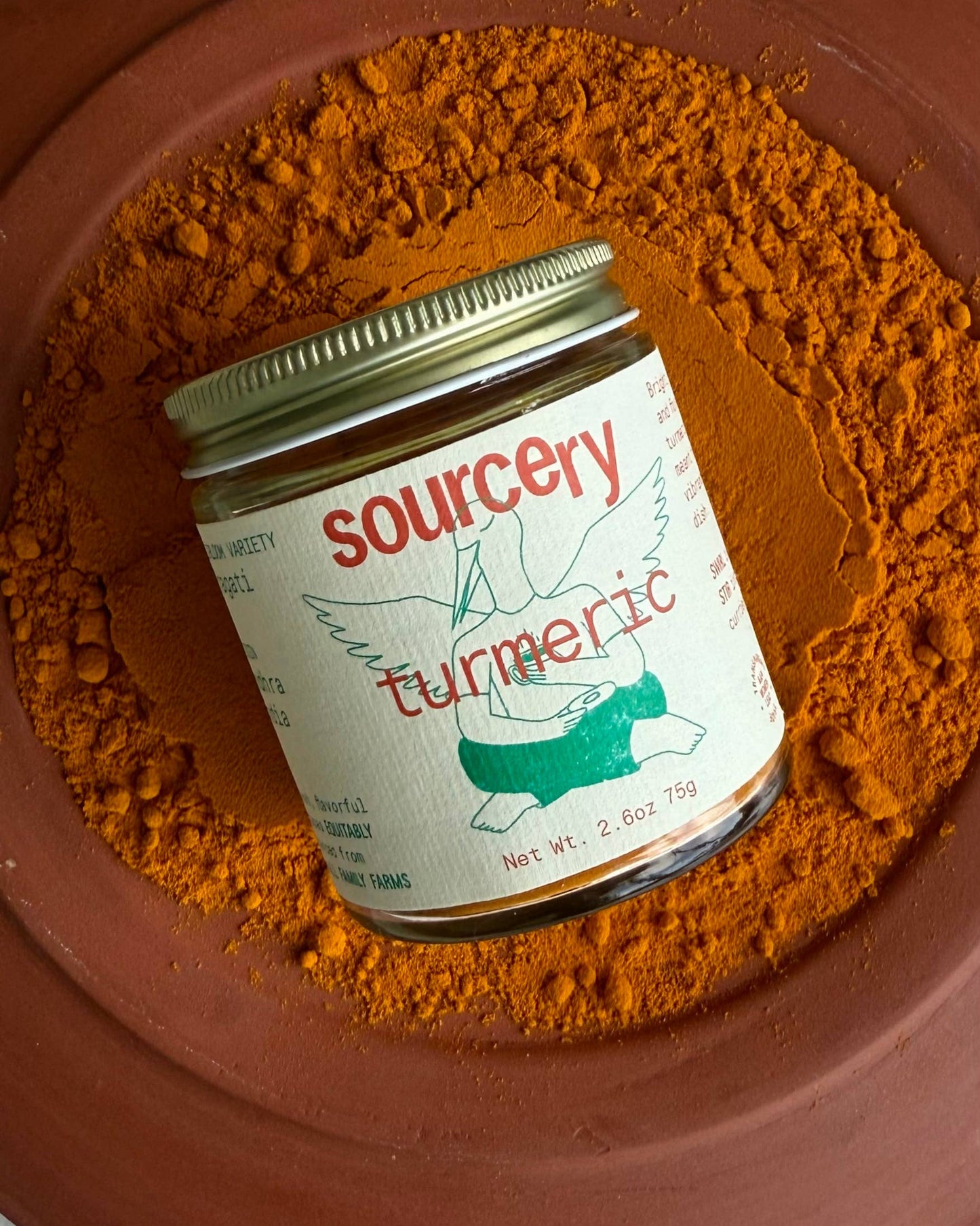 Jar of sourcery turmeric powder on a brown plate with turmeric powder around it.