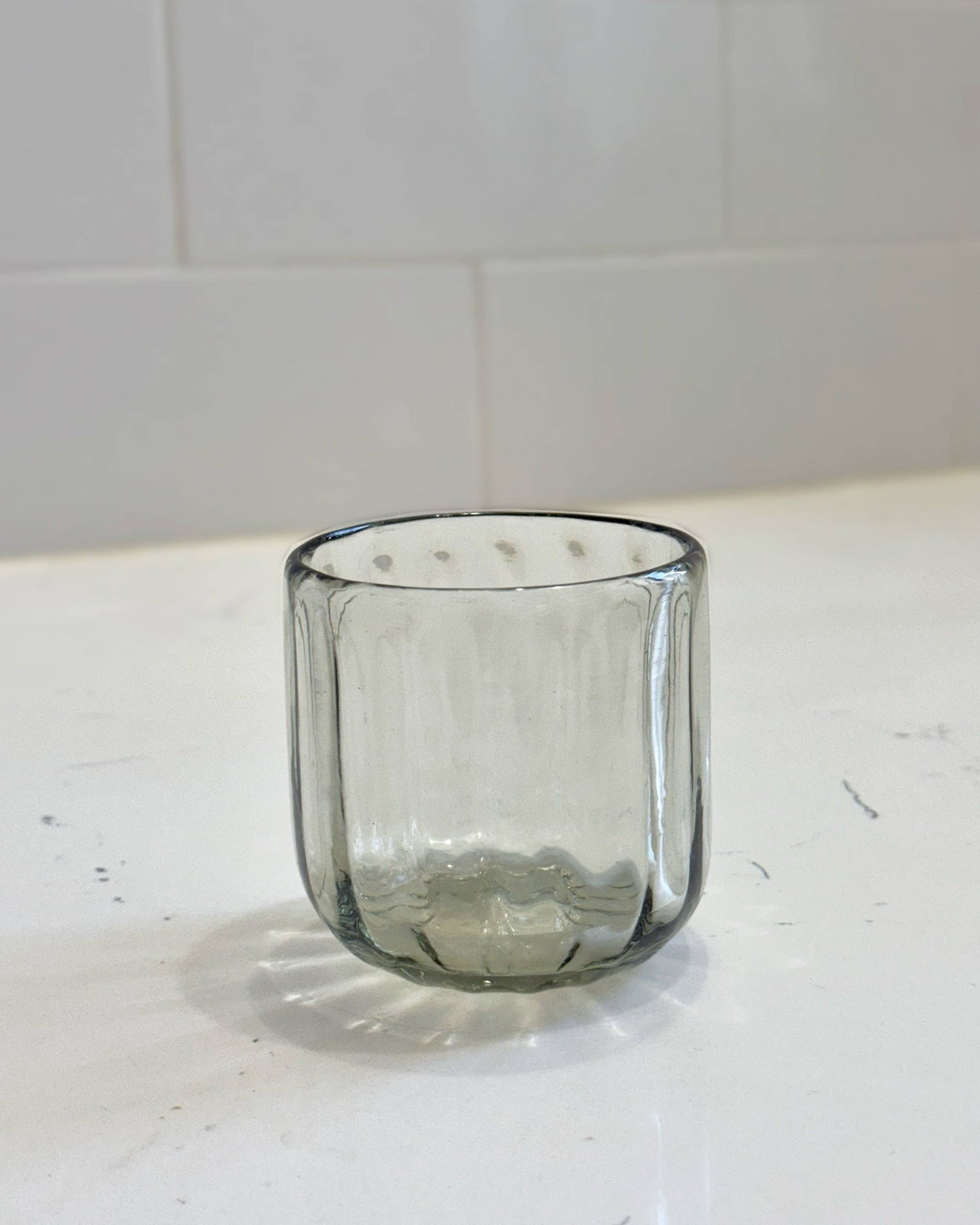 Clear glass tumbler on a white surface with a tiled wall background