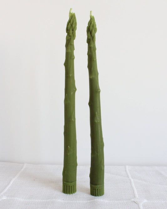 Two green asparagus-like candles on a white surface