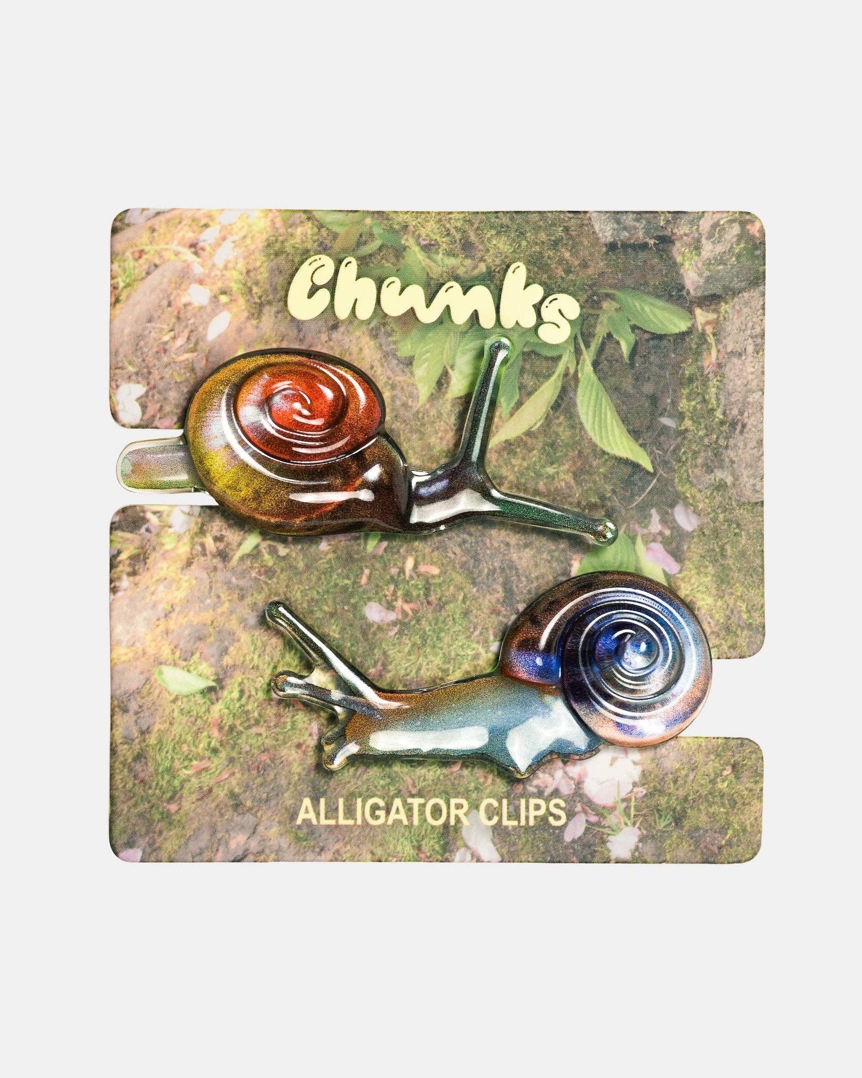 Two glass alligator clips with colorful spiral shells, displayed on their branded cardboard backing labeled 'Chunks' and 'Alligator Clips'.