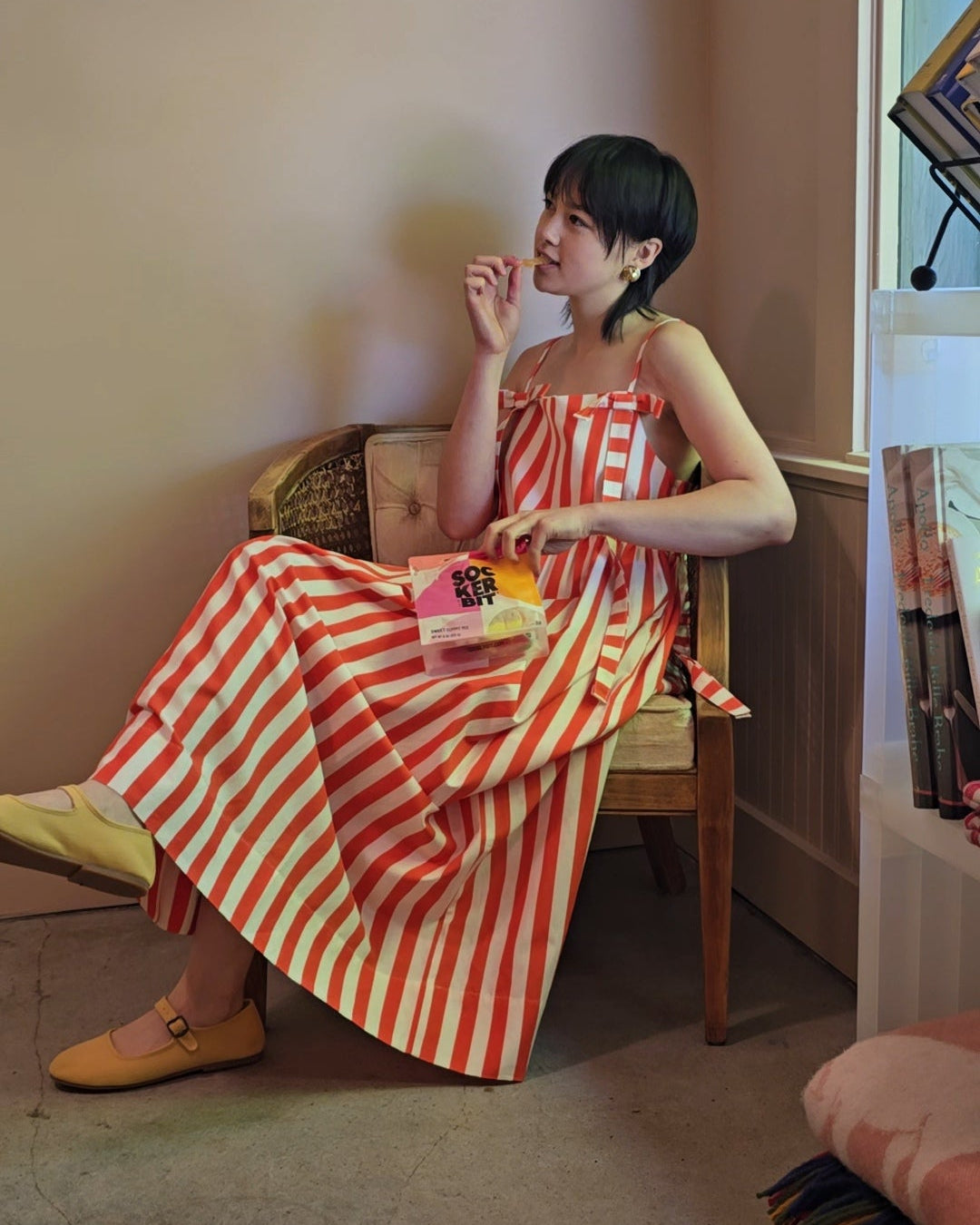 Woman in a red and white striped dress sitting on a chair indoors.