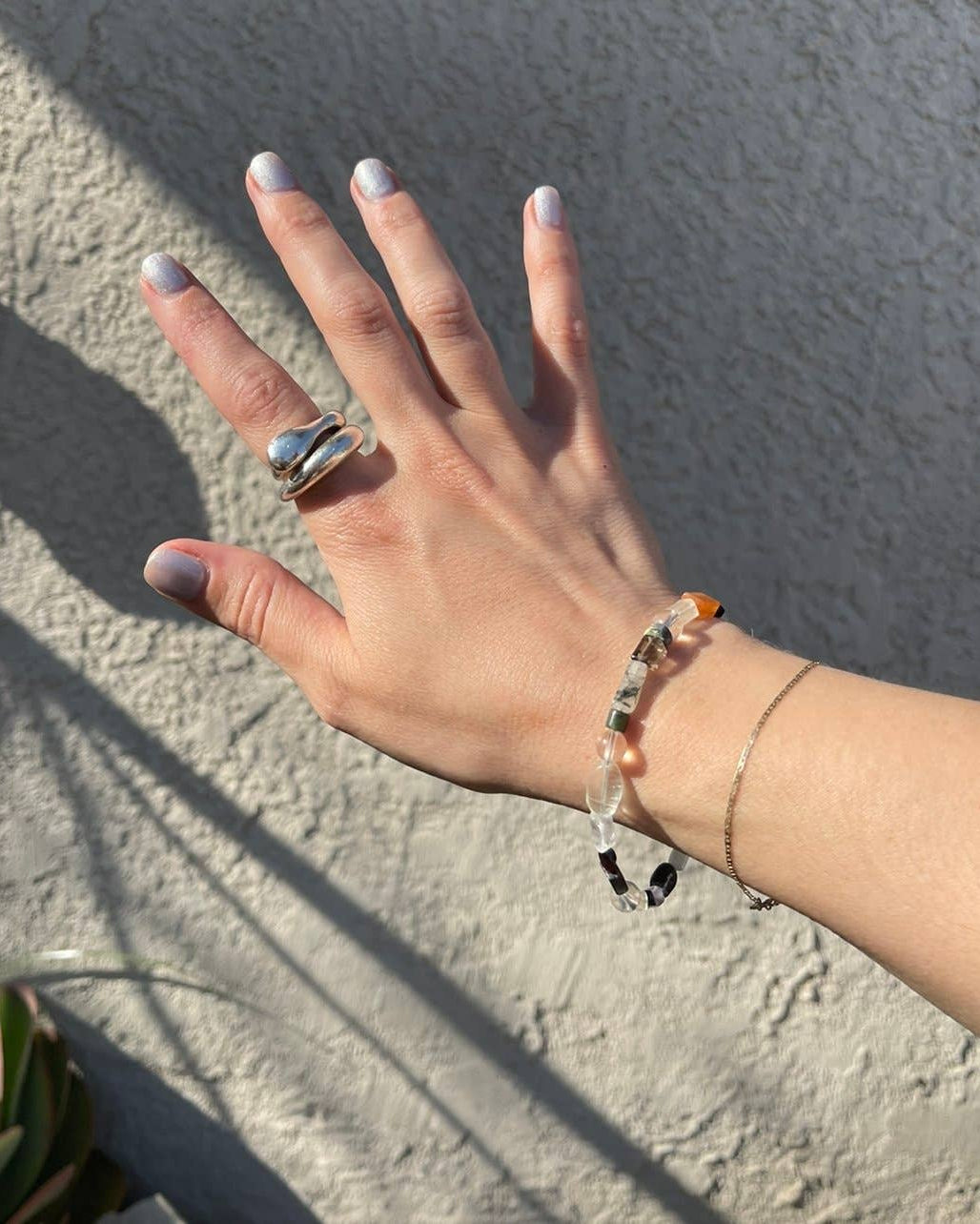 Hand with a ring and bracelets against a textured wall