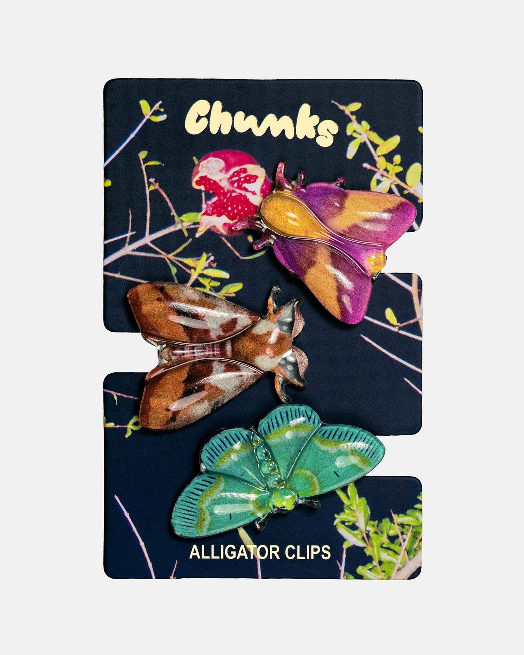 Three colorful enamel alligator clip charms displayed on a dark navy backing card labeled 'Chunks' and 'ALLIGATOR CLIPS'. The clips feature purple, yellow, brown, and green patterns resembling alligator scales and skin.