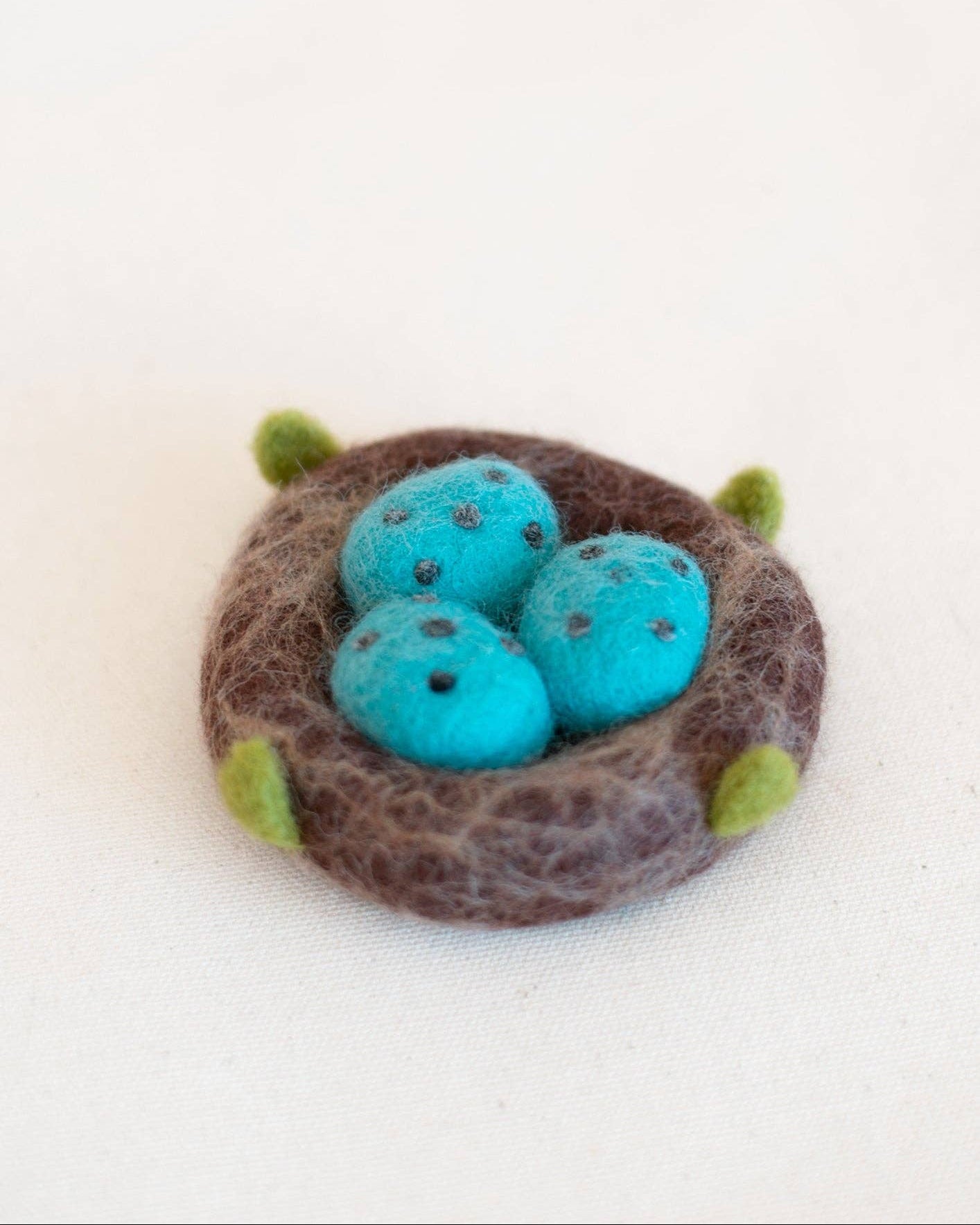 Felted nest with blue eggs on a white background