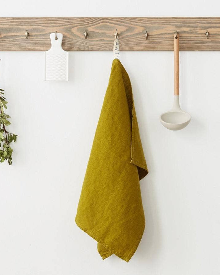 Wooden peg rail with a green towel, plant, and spoon on a white wall.