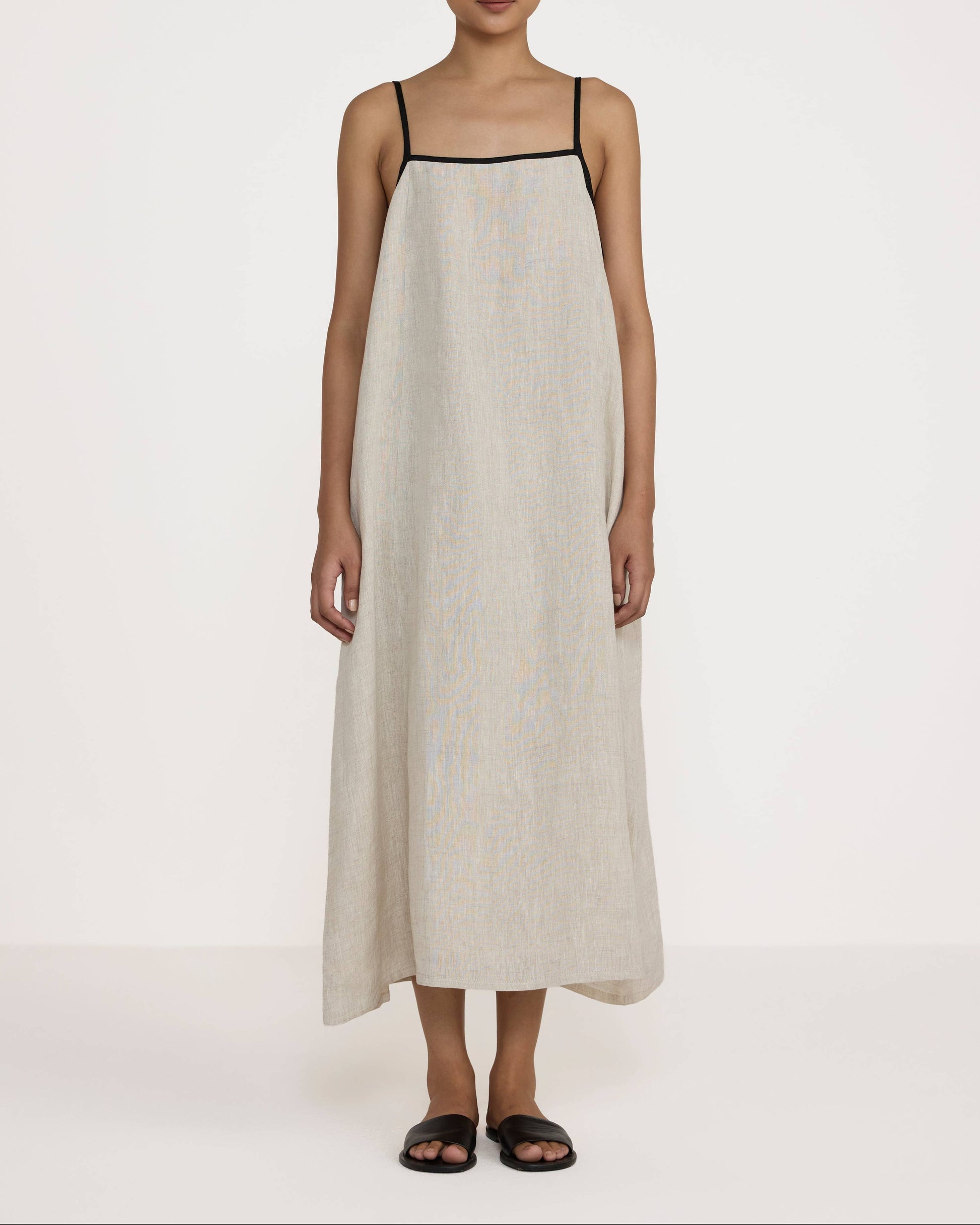 Woman wearing a beige slip dress with black straps on a white background