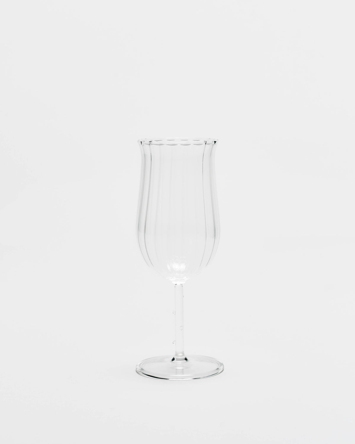 A clear ribbed glass goblet or tumbler with a flared rim and a slender stem, centered on a seamless white background.