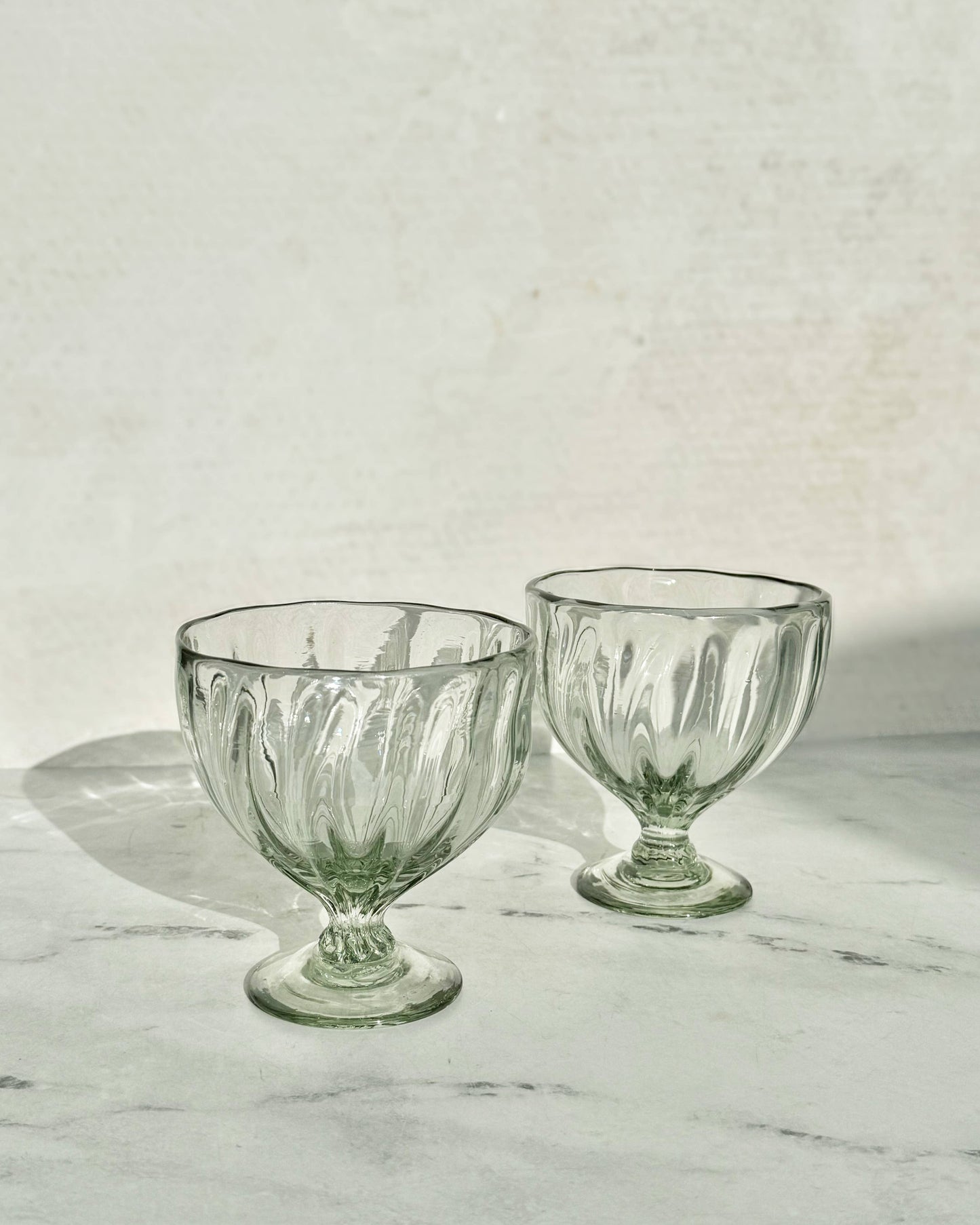 Two clear glass goblets on a marble surface with a light gray background