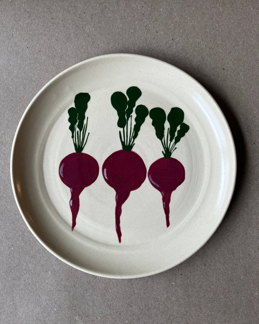White plate with three purple radishes and green leaves on a gray background