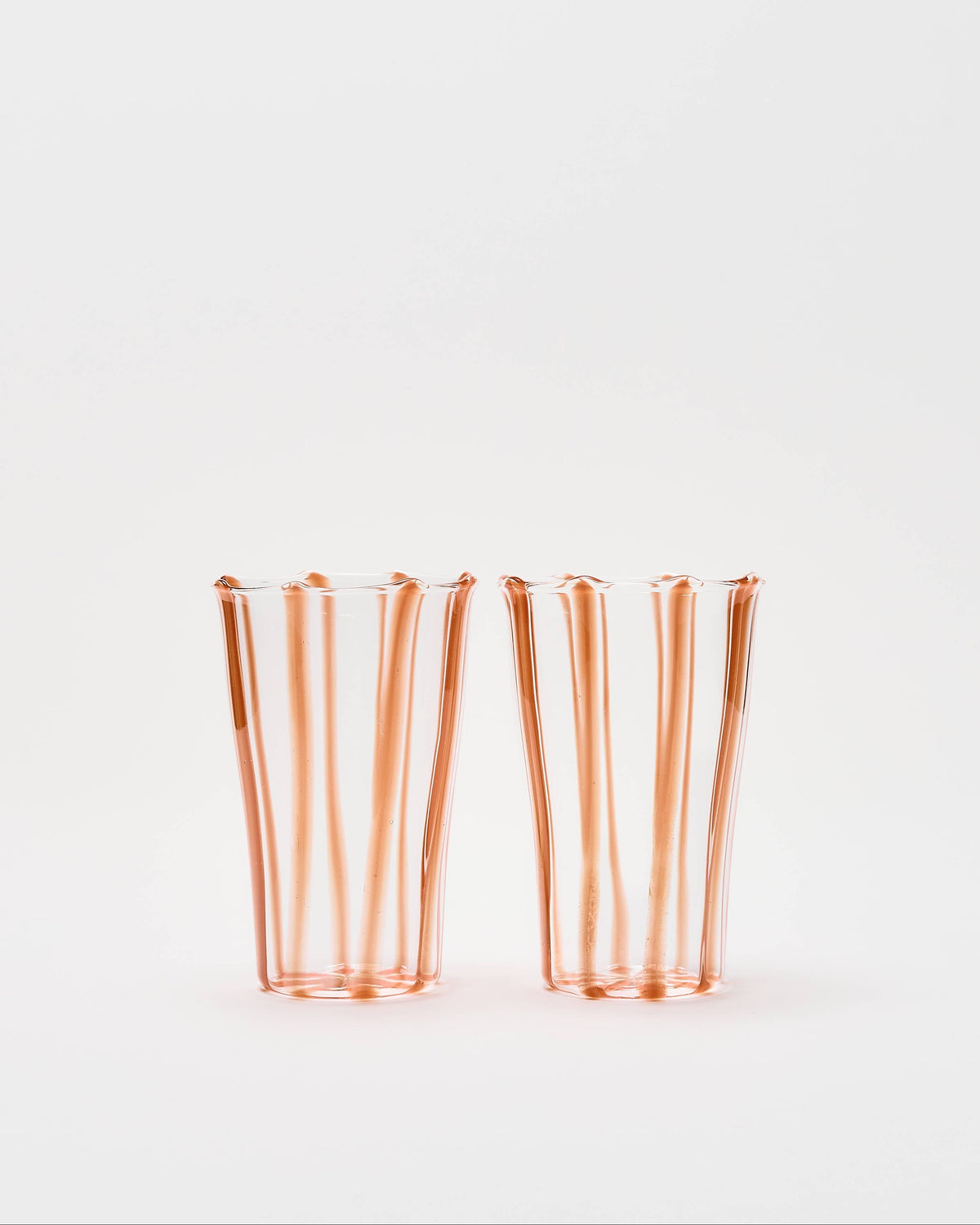 Two clear glass tumblers with vertical flared edges and a warm copper-orange tint, standing side by side on a plain white background.