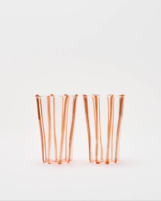 Two clear glass tumblers with vertical flared edges and a warm copper-orange tint, standing side by side on a plain white background.