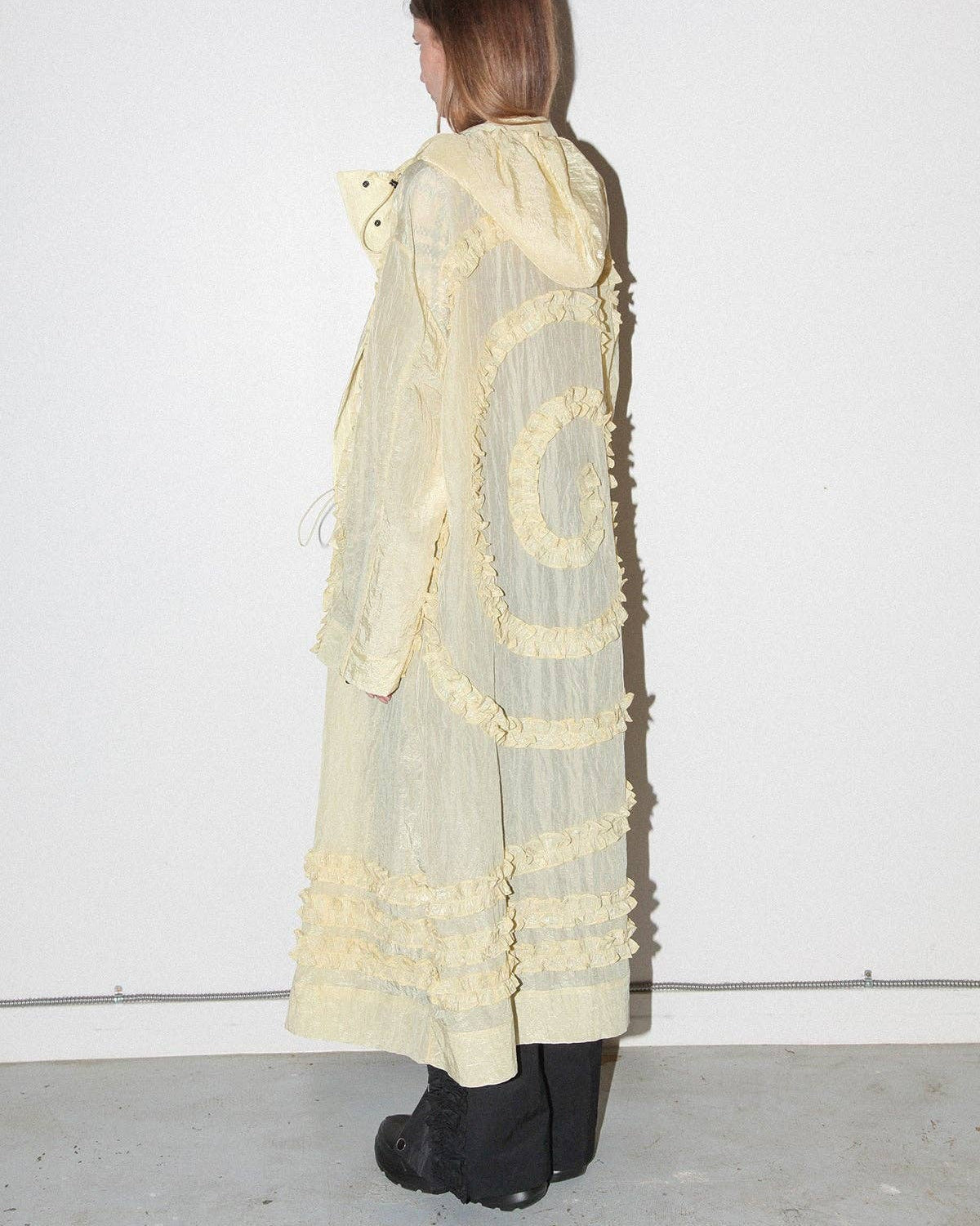 Person wearing a long, light-colored dress with ruffled details against a white background