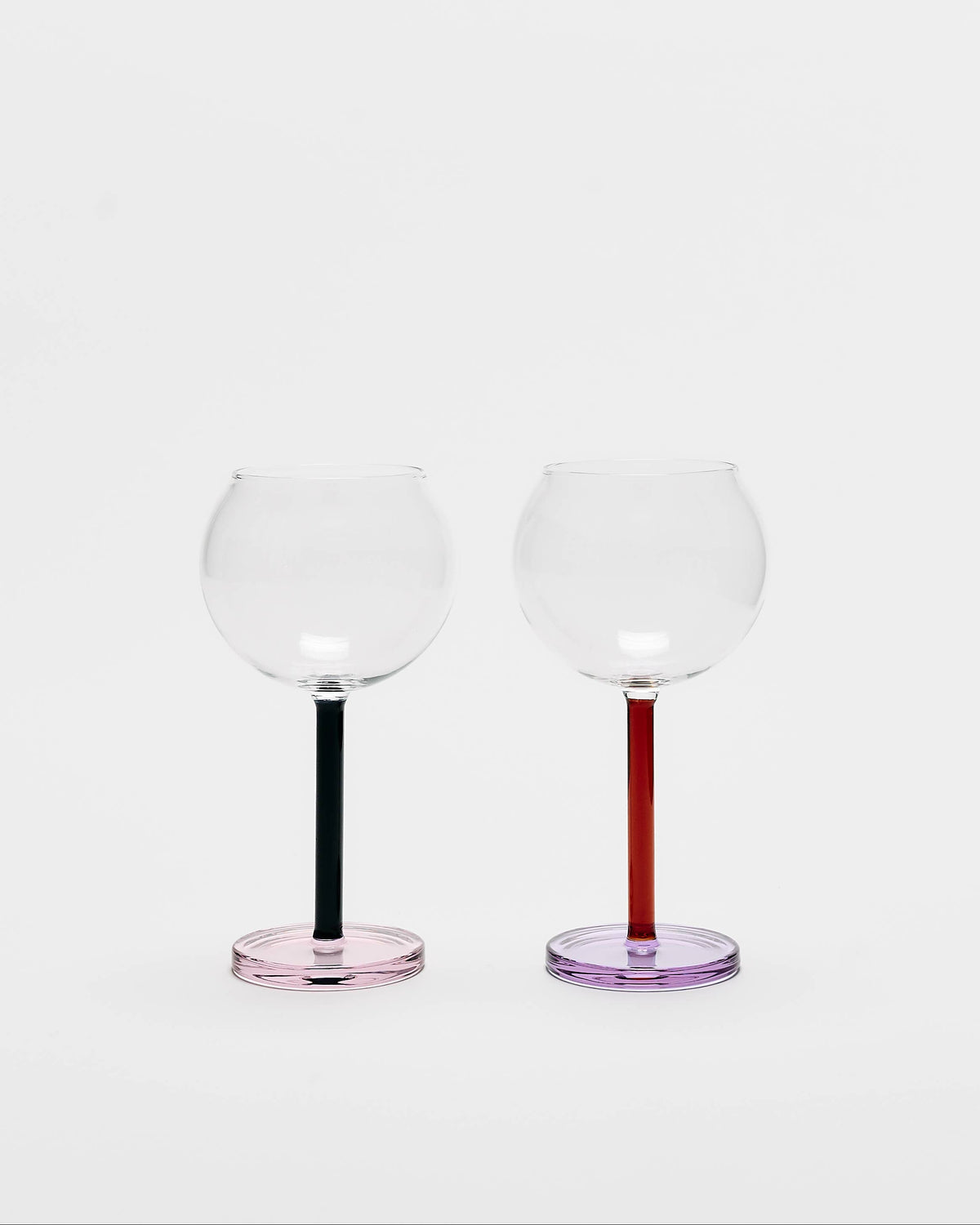 Two clear stemmed wine glasses with colored bases, one with a black stem and pink base, and the other with a red stem and purple base, on a light gray background.
