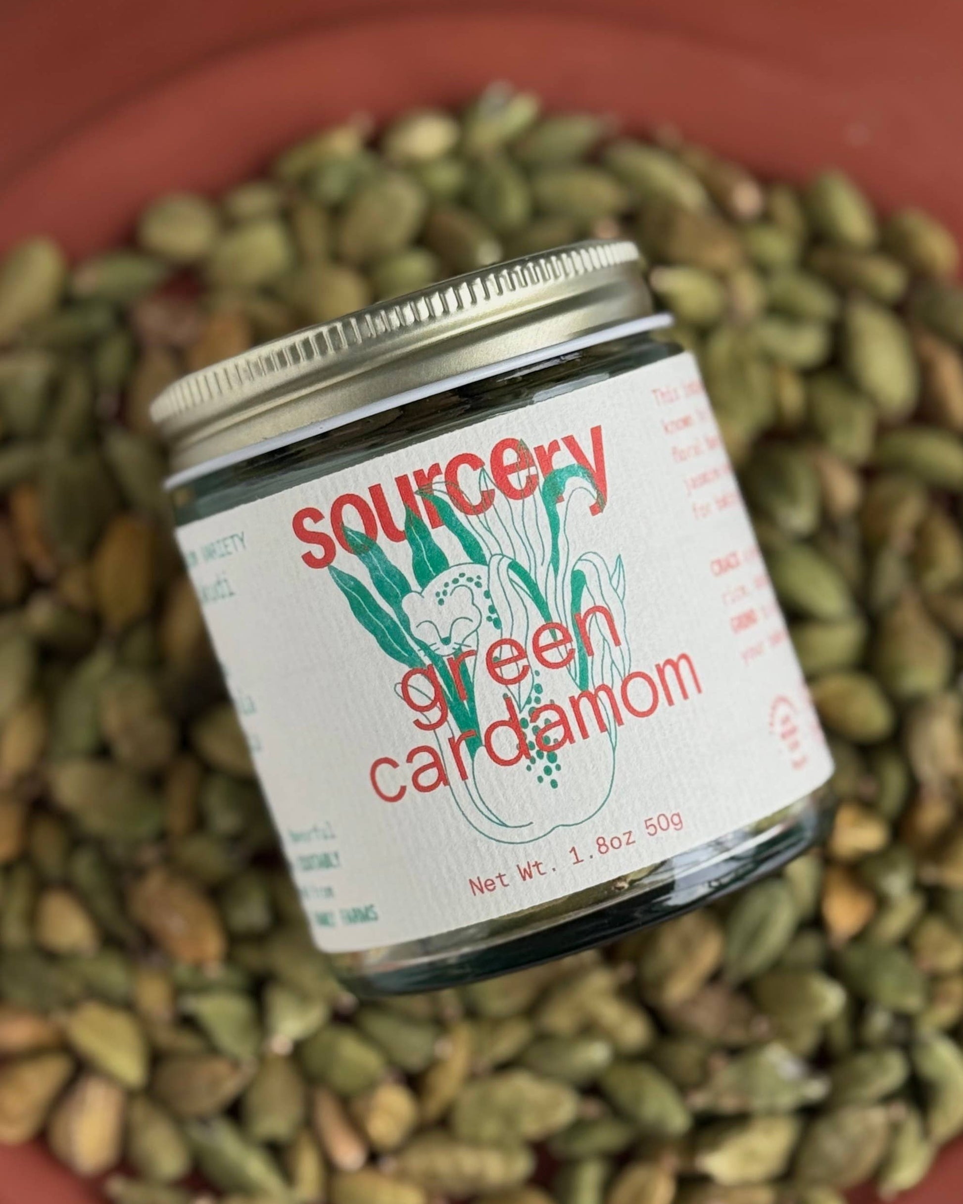 Jar of 'Sourcery Green Cardamom' on a bed of green cardamom seeds.