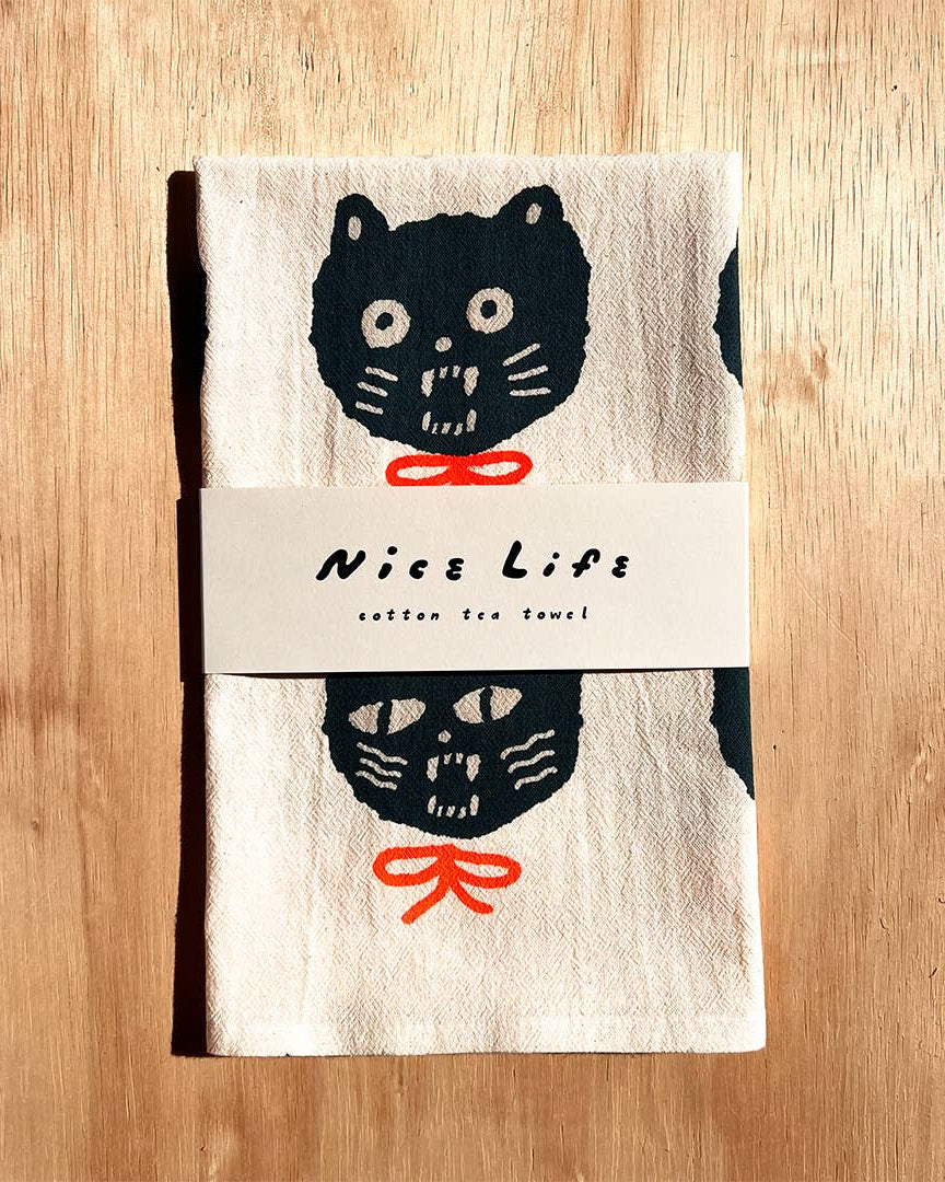 Tea towel with black cat design and 'Nice Life' label on a wooden surface