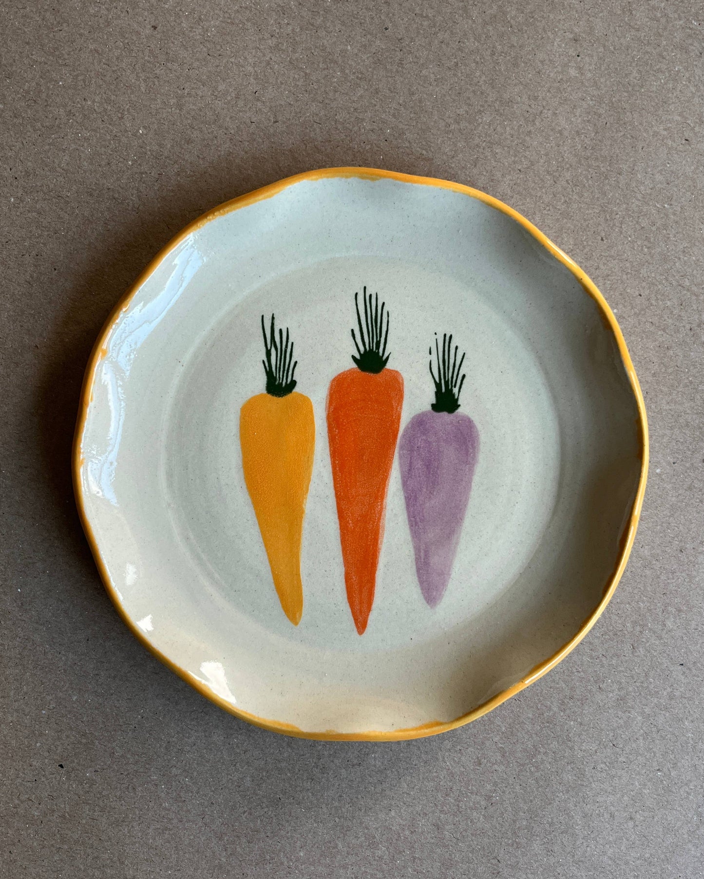 Small plate with three painted carrots on a gray background