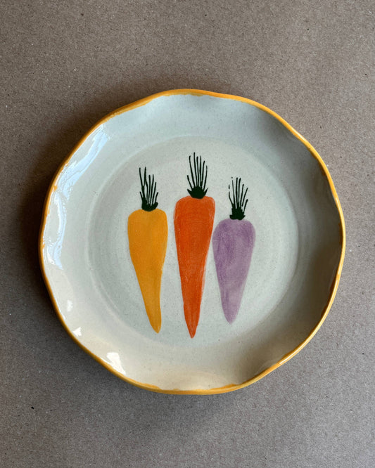 Small plate with three painted carrots on a gray background