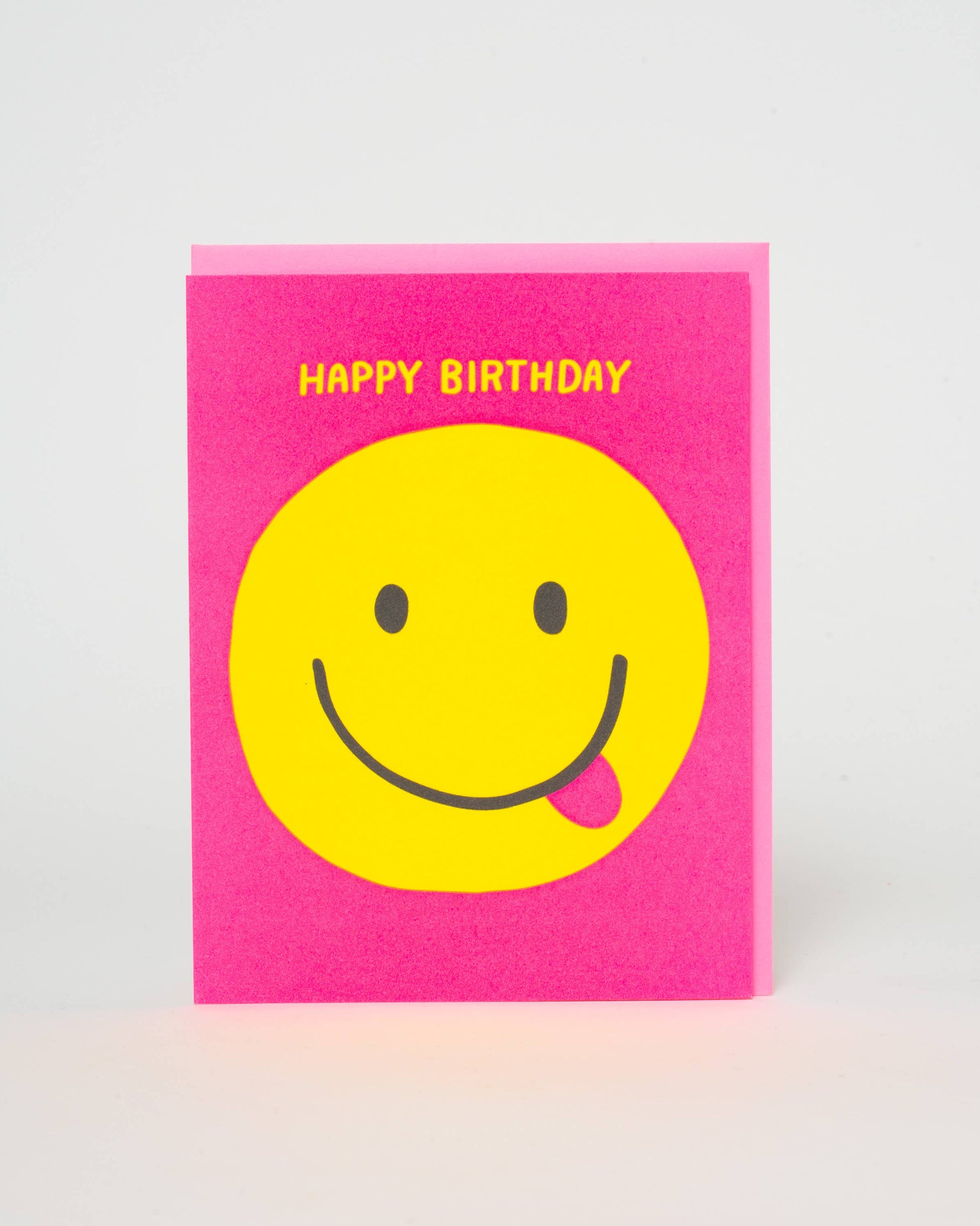 Pink card with a yellow smiley face and 'Happy Birthday' text on a light gray background