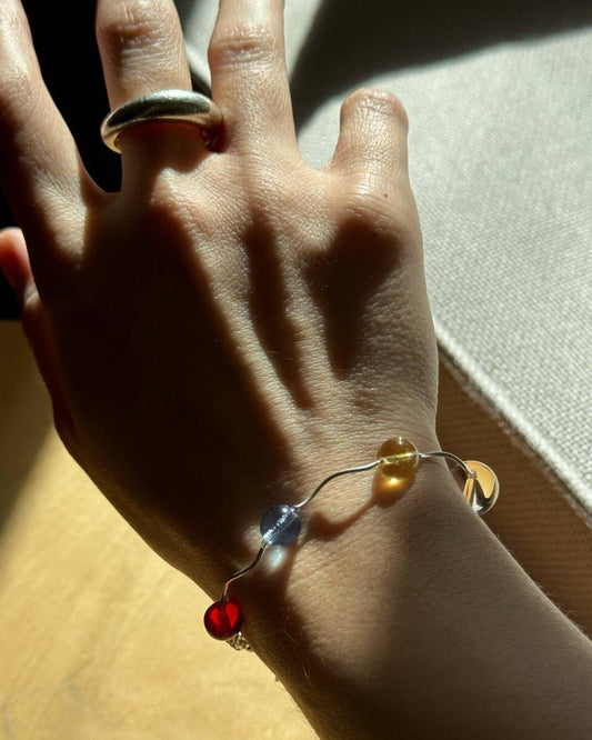 Hand wearing a bracelet with red heart charm on a light background