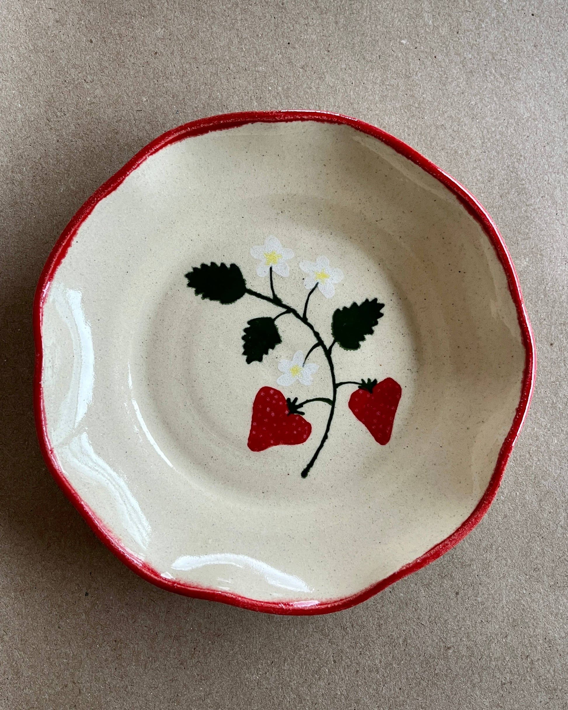 Ceramic dish with red rim and strawberry design on a beige background