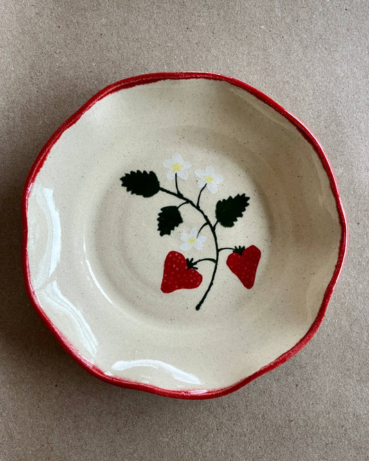 Ceramic dish with red rim and strawberry design on a beige background