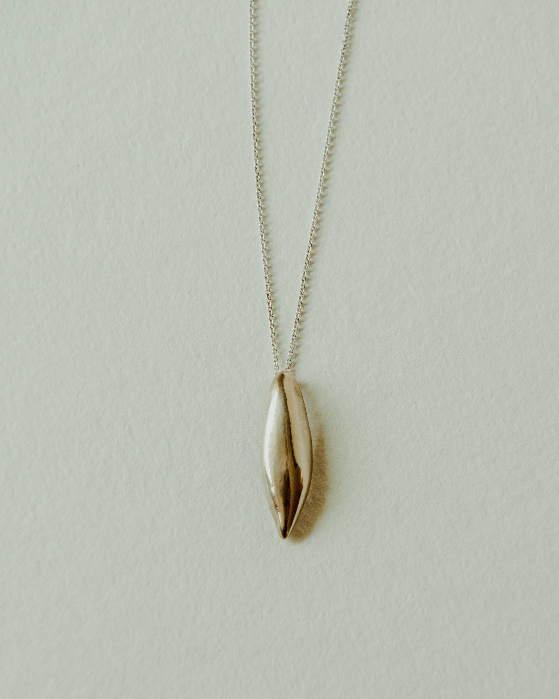 Gold leaf-shaped pendant on a silver chain against a light gray background