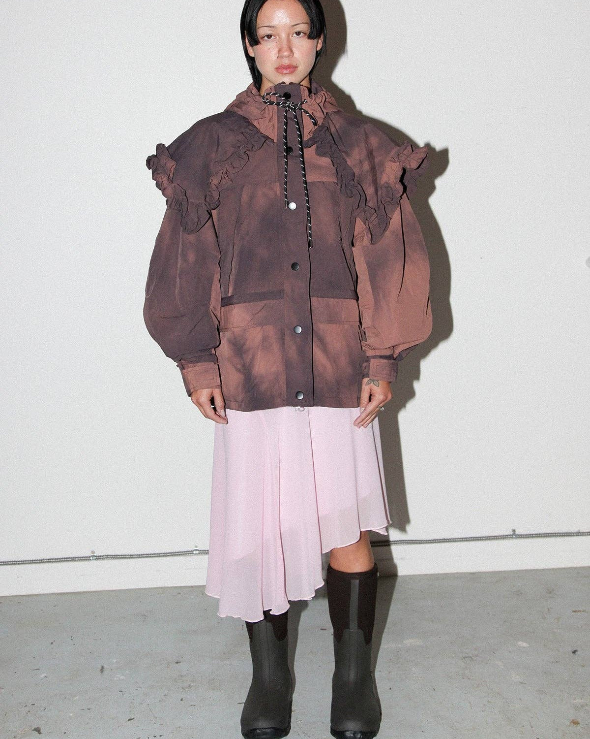 Person wearing a brown textured jacket, light pink skirt, and black boots on a white background