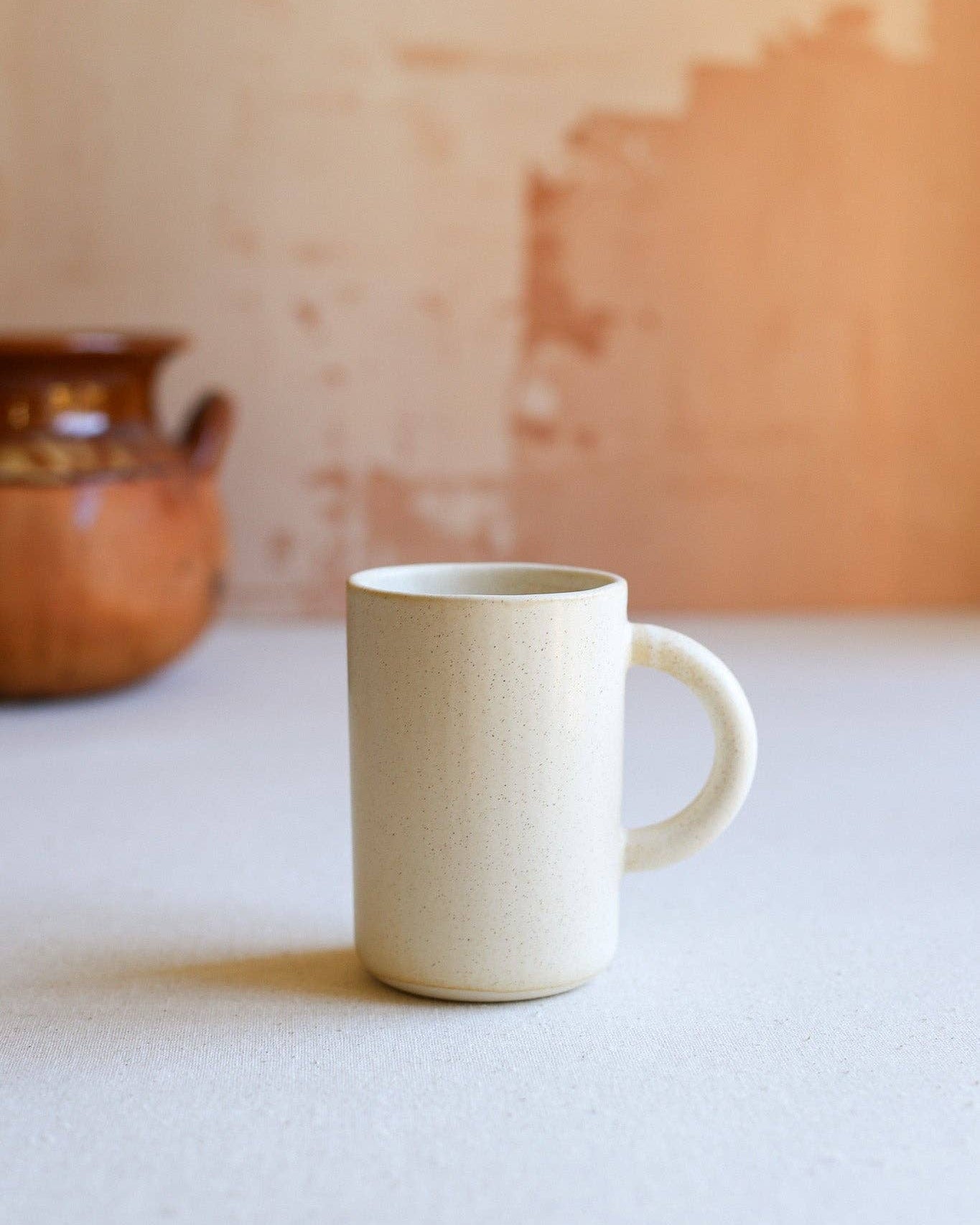 Beige ceramic mug on a white surface with a beige wall in the background