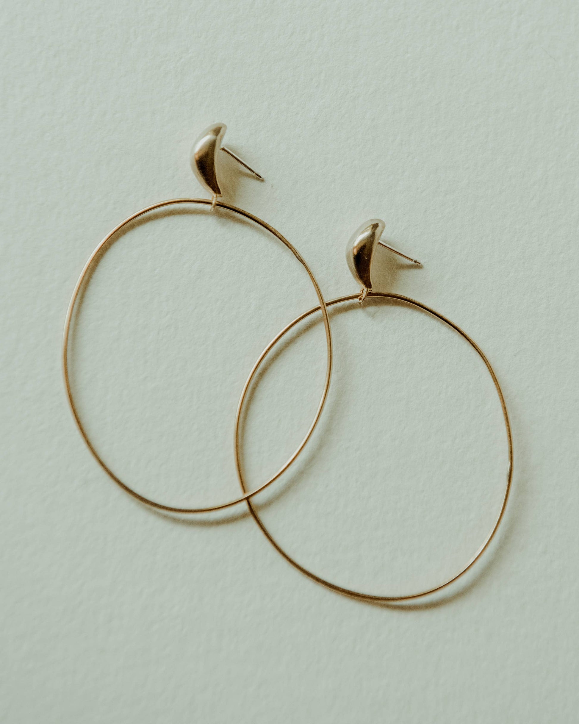 A pair of gold hoop earrings with small curved post backings, displayed on a textured off-white background.