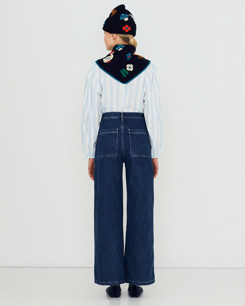 A model shown from the back wearing a white and blue striped long-sleeve shirt, dark blue wide-leg denim jeans, a black knit beanie with colorful floral embroidery, and a dark navy bandana with embroidered details.
