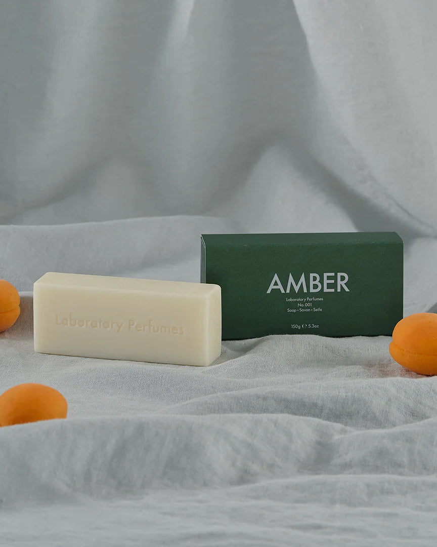 Bar of soap with a green box labeled 'AMBER' on a textured surface with apricots.