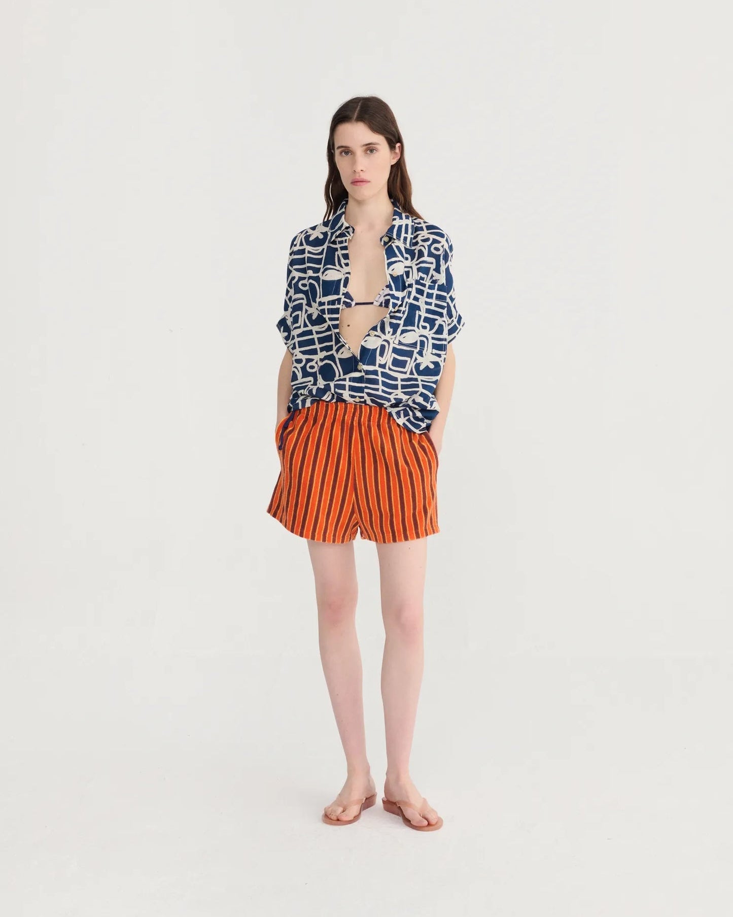 Woman wearing a patterned shirt and striped shorts on a white background