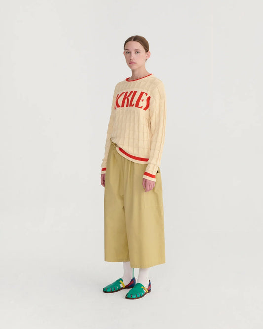 Person wearing a beige sweater with red text and beige pants on a white background