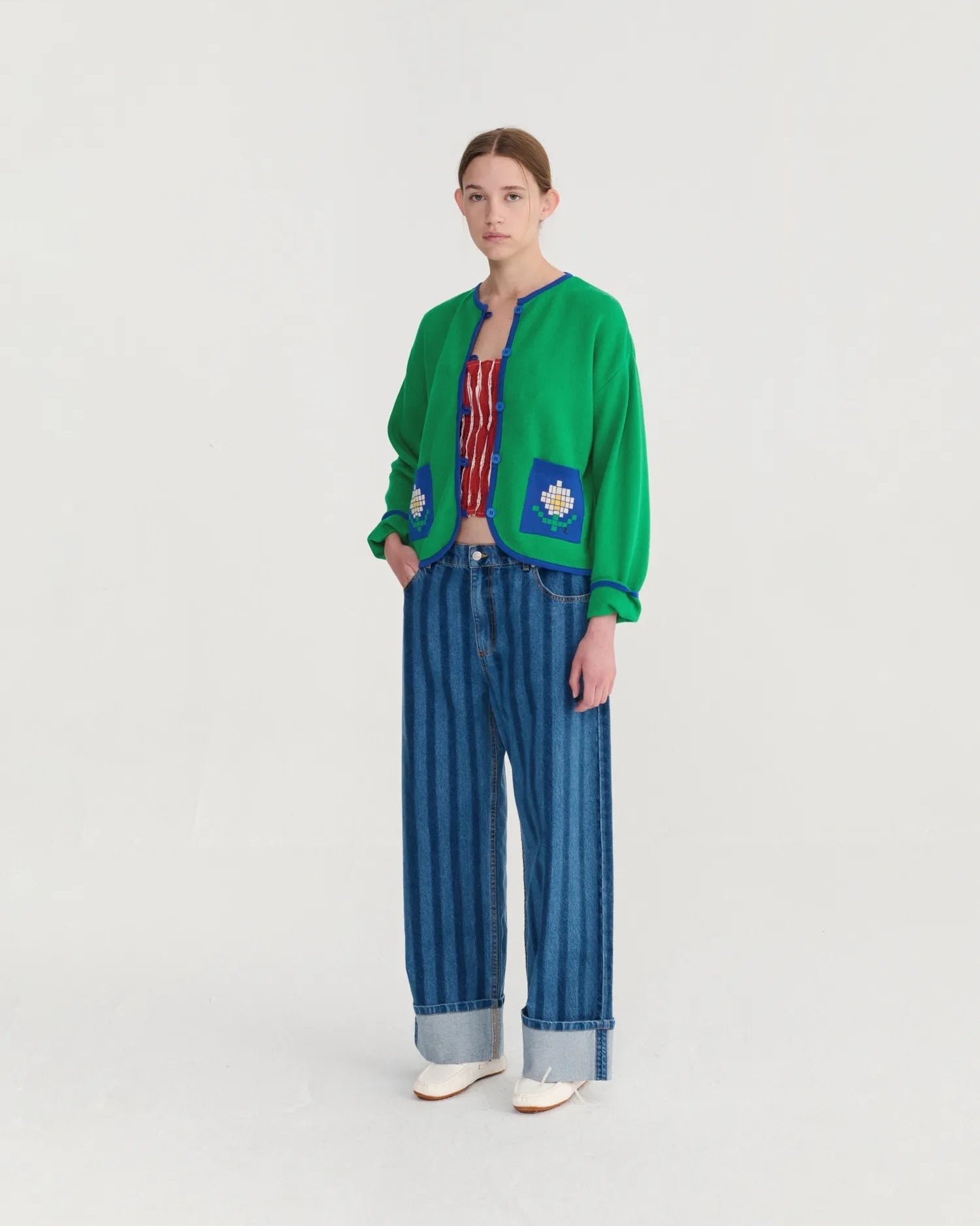Person wearing a green cardigan with floral patterns and blue striped pants on a white background
