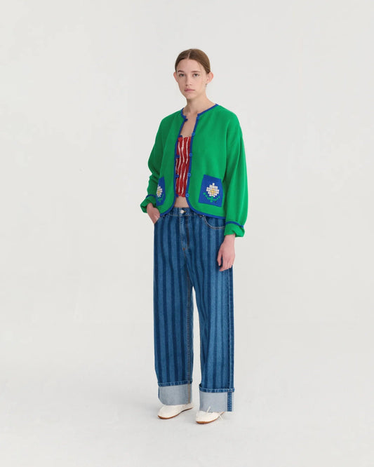 Person wearing a green cardigan with floral patterns and blue striped pants on a white background