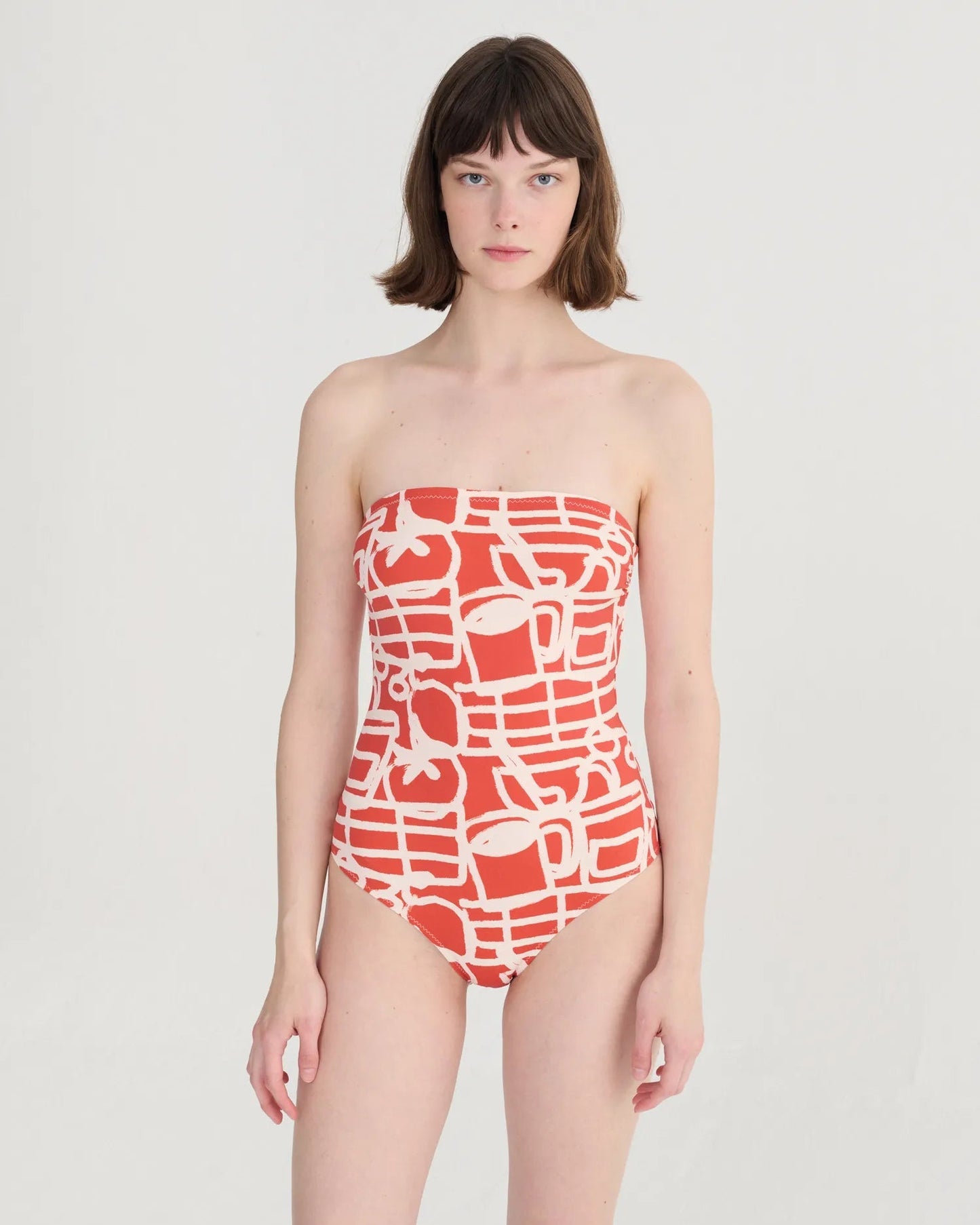 Woman wearing a strapless red and white patterned swimsuit on a light gray background