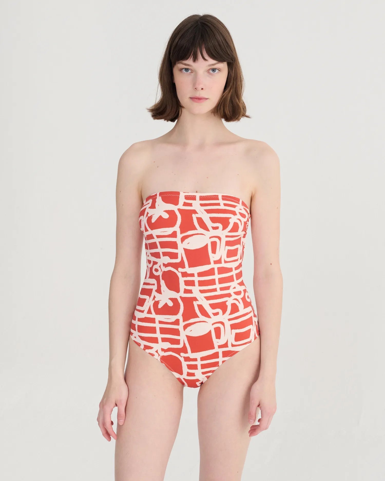 Woman wearing a strapless red and white patterned swimsuit on a light gray background