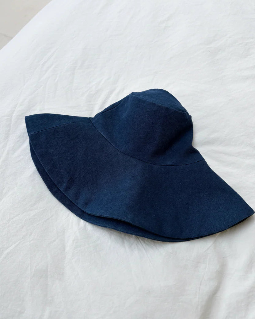 A dark navy blue wide-brim sun hat resting on a white fabric surface.