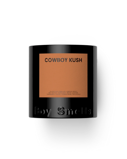 Candle with 'Cowboy Kush' label and 'Boy Smells' branding on a white background