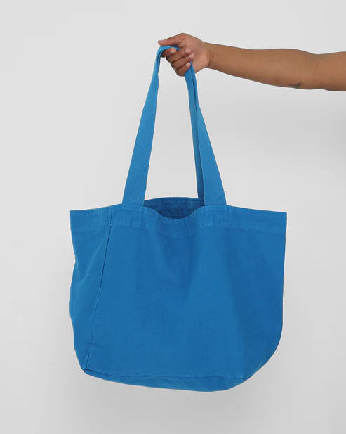 Blue tote bag held by a hand against a white background