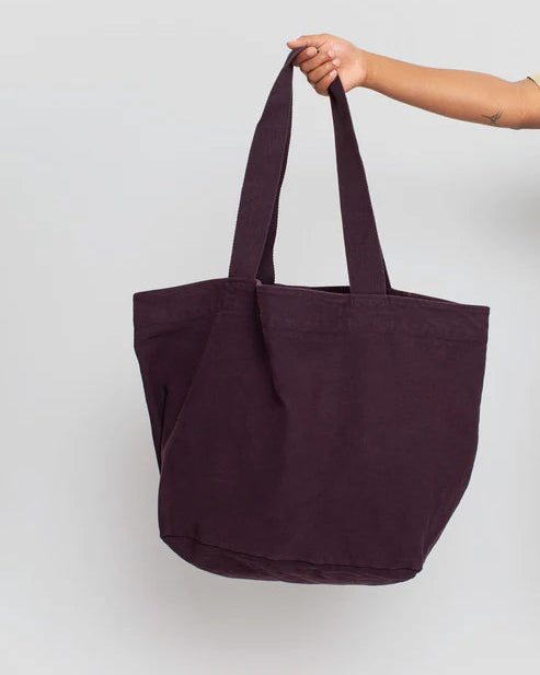 Person holding a dark purple tote bag against a light gray background