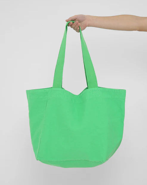 Green tote bag held by a hand against a white background