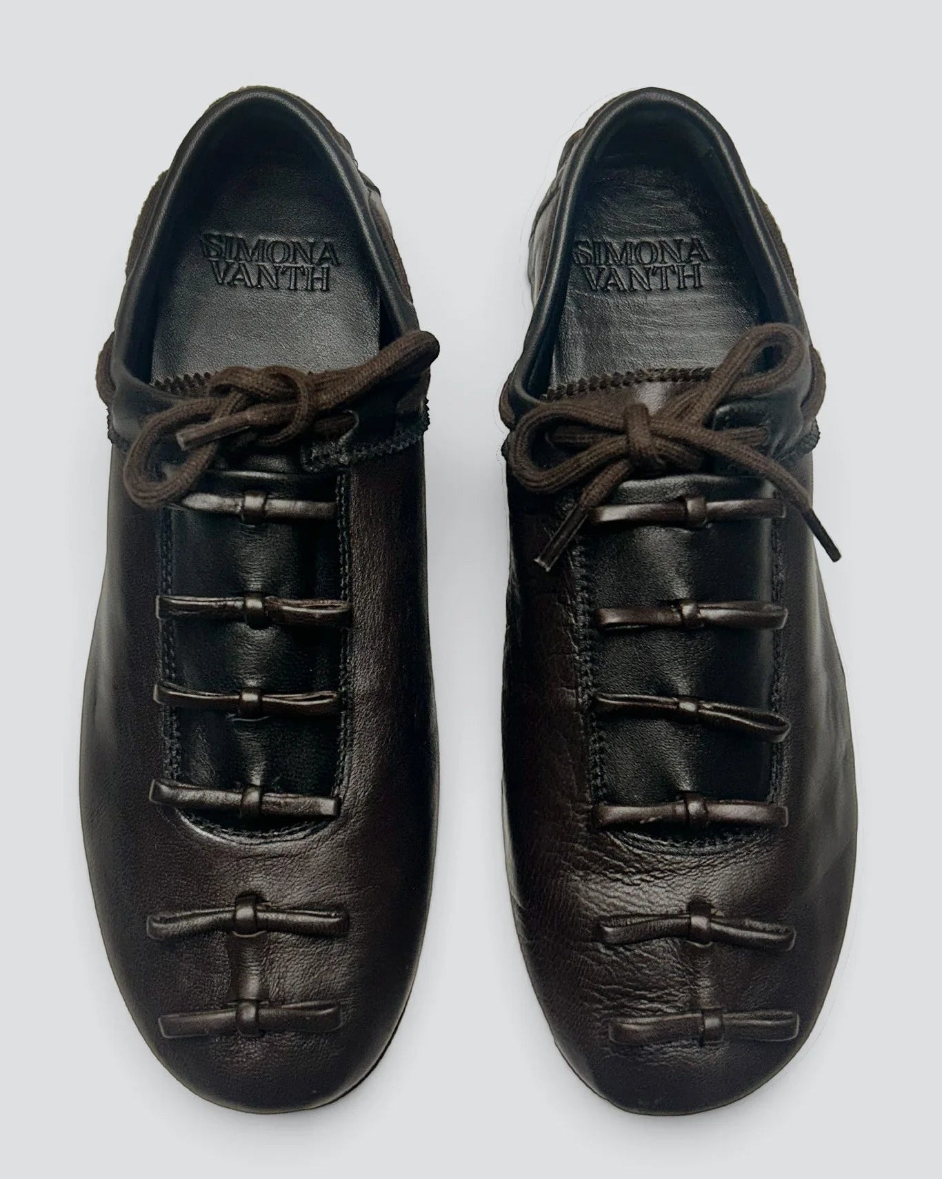 A pair of dark brown leather lace-up shoes with unique toggle closures on the front, shown from a top-down view on a light gray background. The brand name 'SICILIA MANITI' is visible on the insole of each shoe.