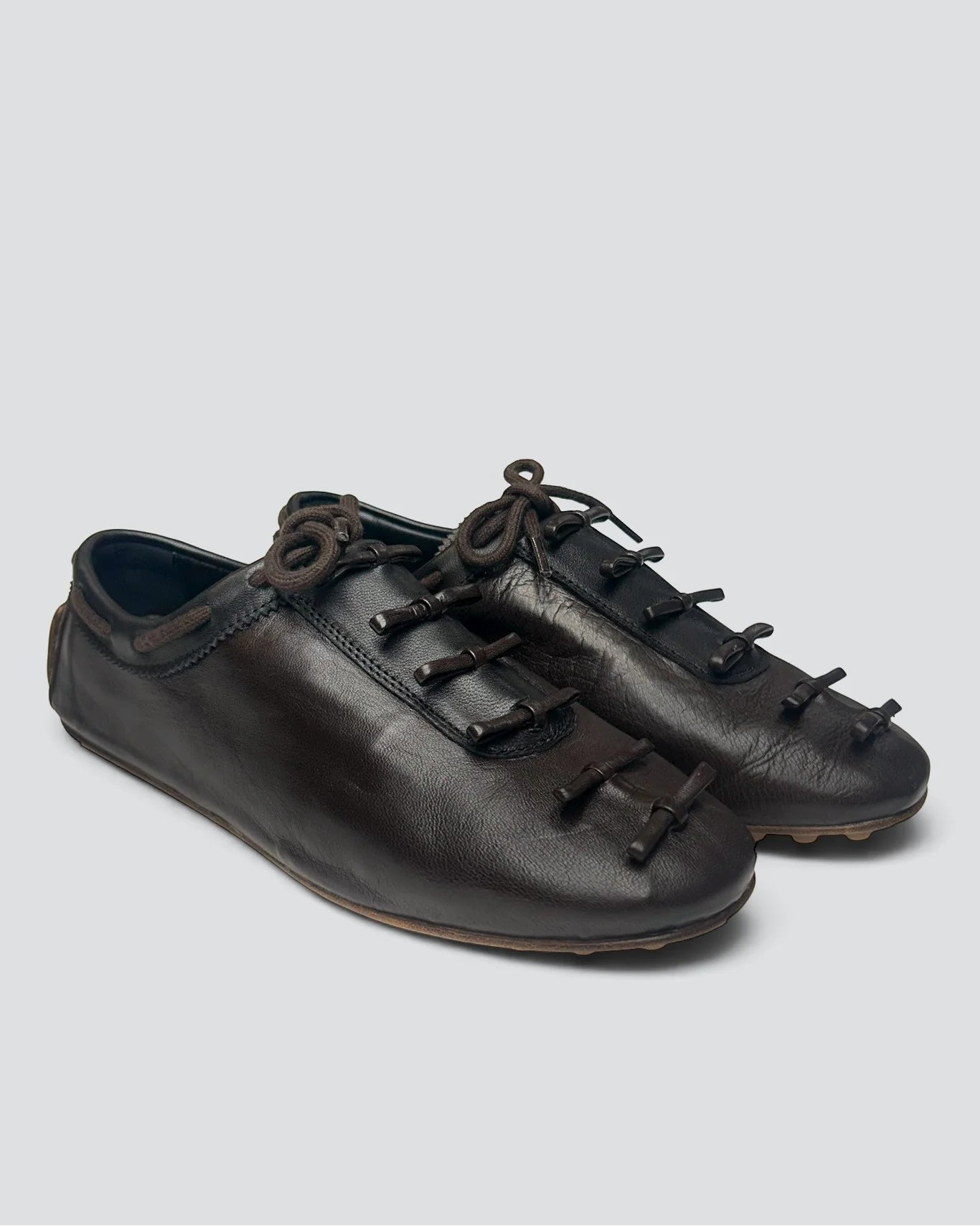 A pair of dark brown leather lace-up shoes with decorative toggle details on the toe, shown against a solid light gray background.