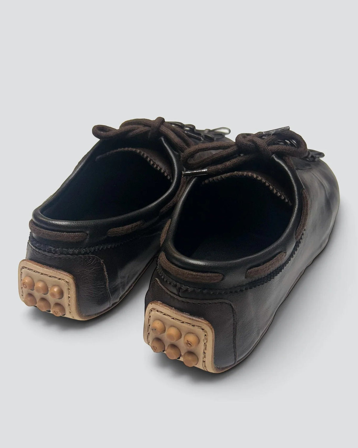 A pair of dark brown leather slip-on shoes with textured beige heel pads featuring raised circular bumps, photographed on a light gray background.