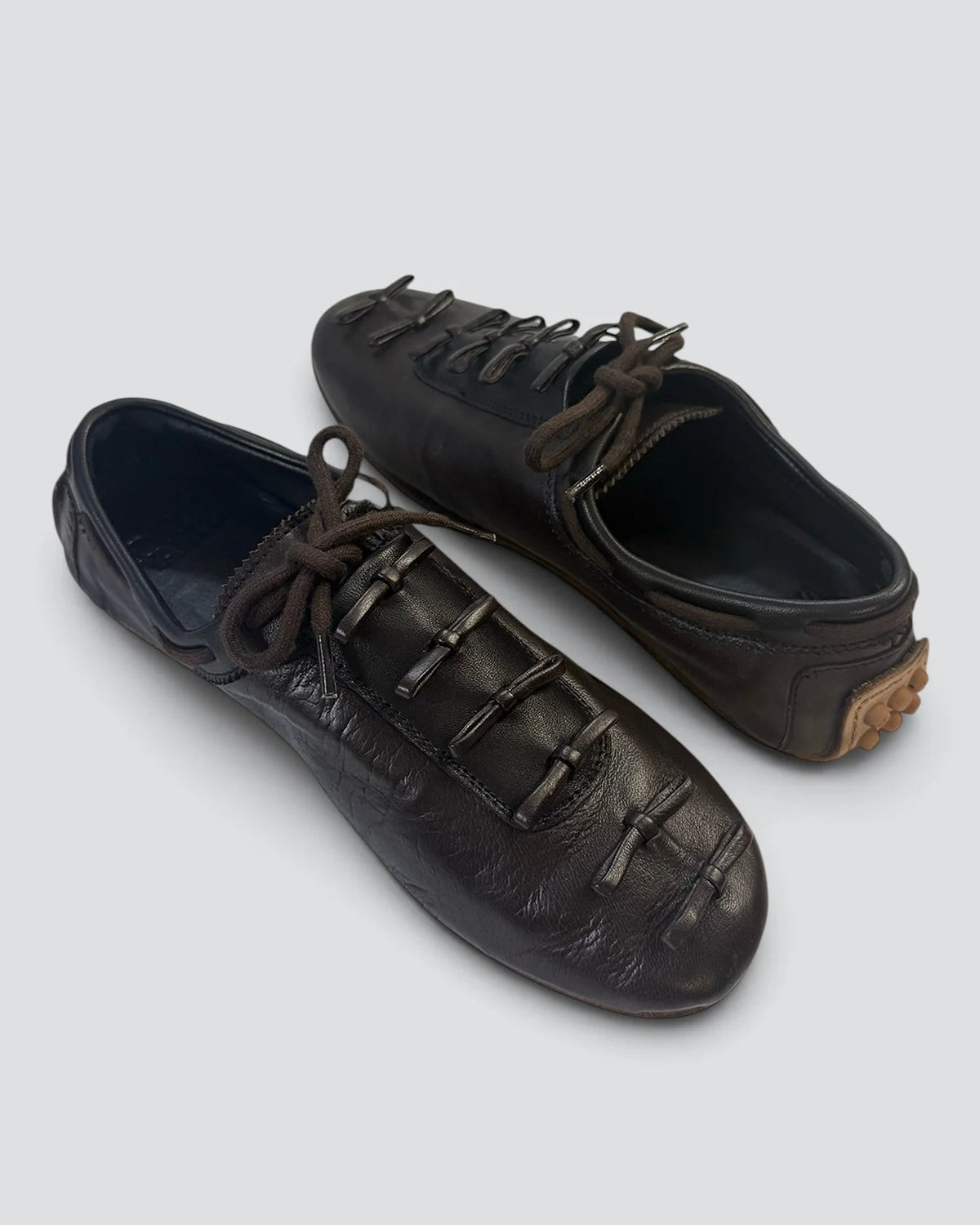 A pair of black leather lace-up shoes with decorative strap details across the toe, displayed on a light gray background.